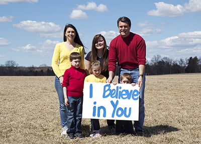 Katie and family holding a sign that says: "I Believe in You"